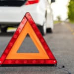 triangolo segnale di pericolo stradale davanti ad un 'automobile in panne in mezzo alla strada