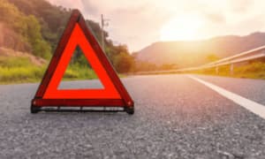 triangolo per pericolo stradale in mezzo ad una strada deserta col tramonto sullo sfondo
